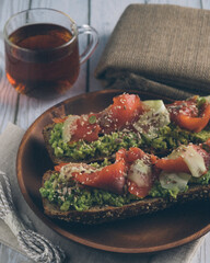 Bruschetta with salmon and avocado on a wooden plate on a white wooden background.