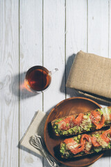 Bruschetta with salmon and avocado on a wooden plate on a white wooden background.