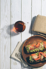 Bruschetta with salmon and avocado on a wooden plate on a white wooden background.