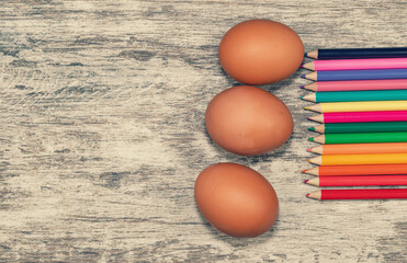 Easter background on a wooden surface with unpainted eggs and colorful pencils