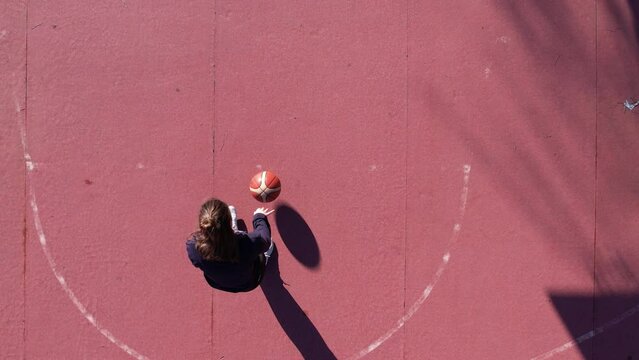Santo Tirso, Portugal - January 1, 2022: DRONE AERIAL FOOTAGE SLOW MOTION - A young girl basketball player training and exercising outdoors on the local court. Dribbling with the ball.