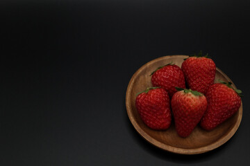 A space with a pitch-black background, lots of strawberries served in a wooden bowl.