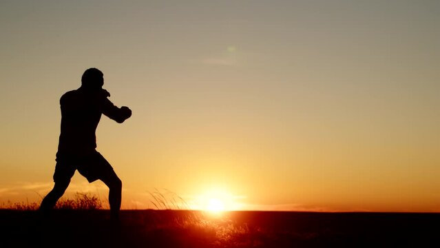 Silhouette black man athlete struggles shadow fight background of sunset, front view. Male athlete trains martial arts punches outdoors. Man trains boxing punch outdoor