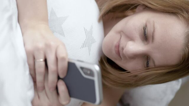 Vertical view beautiful woman are using smart phone on the bed in morning. Female surfing net with cellphone at home. Girl communicate with a friend on her mobile phone.