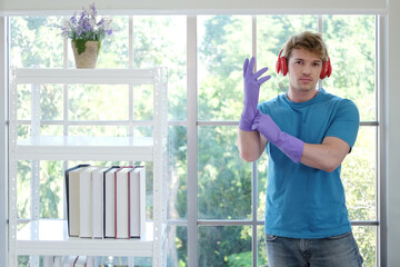 Young Caucasian male Wearing violet rubber gloves for clean of housework and relaxing for listening to music with red headphone. Lifestyle of Familyman on Holiday Concept.