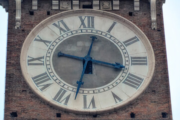 Big tower clock at bell tower of old church in downtown Verona, Italy.