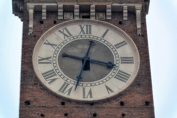 Big tower clock at bell tower of old church in downtown Verona, Italy.