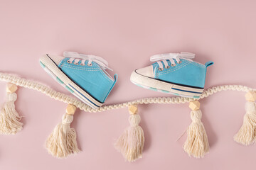 Kid's light blue sneakers on a pastel background with a garland of macrame. A tender childhood...