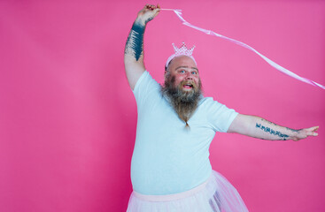 Funny man dancing and having fun wearing  a ballet outfit. Happy princess on a pink colored background