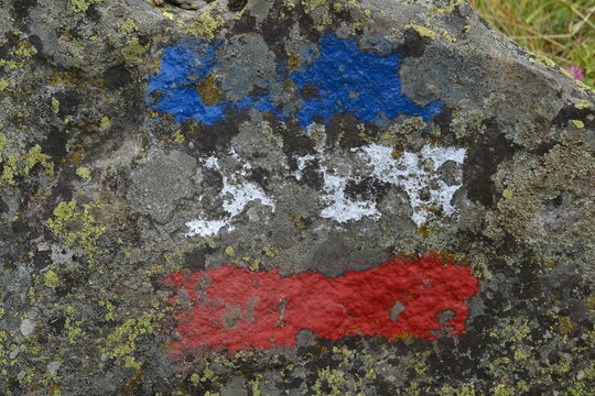 route sign of a mountain tour on a stone in the clors of the French flag in nature area Parc des Ecrins