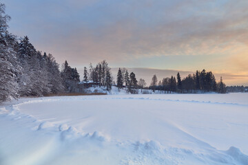 Winter sunset near the Finnish Tuusula lake: shore, snow on ice as oval, nature of northern Europe, coniferous forest.