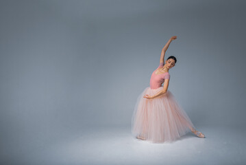 Fototapeta na wymiar young pretty, fragile, beautiful ballerina dancing in a long pale pink dress with a tulle on a uniform background, low key. Ballet, dancing, dancer