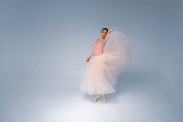 Fototapeta na wymiar young pretty, fragile, beautiful ballerina dancing in a long pale pink dress with a tulle on a uniform background, low key. Ballet, dancing, dancer