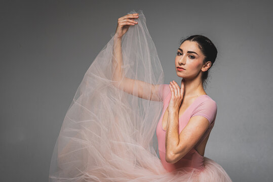Portrait of emotional ballerina. A young elegant ballet dancer, dressed in professional clothes and a pink weightless skirt with a photo, demonstrates her dancing skills and hand movements. 