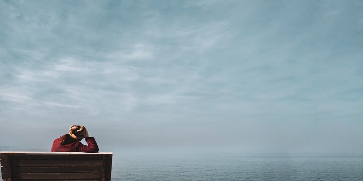 Unhappy single woman sitting on bench, looking at distant sea or seascape horizon. Lonely young woman missing someone, desire or hope to go far away concept idea. Time to go, say goodbye or good bye.