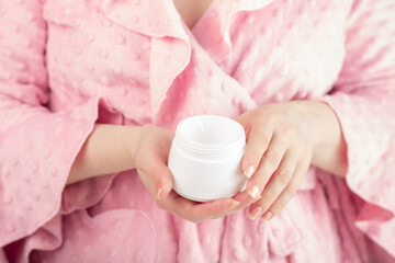 Fototapeta na wymiar lotion for hands, cream for face and body moisturizing is held by a woman in a bathrobe in the bathroom