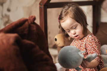 cute girl with down syndrome at home in the bedroom on the bed plays with toys
