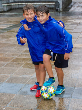 Dos hermanos abrazados con un bal&oacute;n de futbol bajo la lluvia