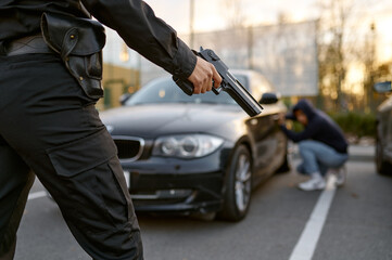Fototapeta na wymiar Policewoman holding gun at car thief backview