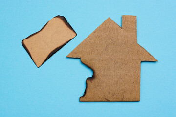 Burned paper house model on blue background. Home insurance concept.