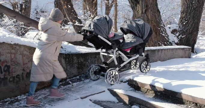 Mother struggling pushing baby stroller for twins going up the ramp in the snow