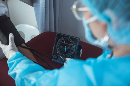 A Nurse In Full PPE Gear Inflating A Cuff To Check The Blood Pressure. Using A Sphygmomanometer. At The ER Or Emergency Room Of A Hospital.