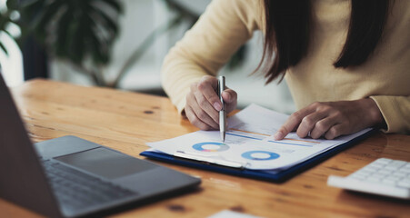 Close up Businesswoman hand holding pen and pointing at financial paperwork, financial charts to analyze profit concept