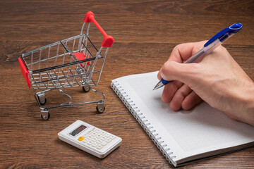 Budget calculation. Man calculates the budget. Shopping cart a on table with calculator and paper....