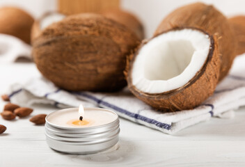 Soy natural candle with coconut aroma in a metal candlestick against the background of an open coconut with pulp. Composition on gray cement. Organic product. Side view.