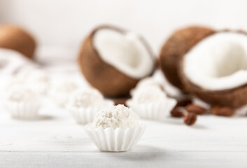 Coconut candies. Coconut balls in a light package on a white textured wood. Homemade vegan sweets.Closeup view, place for text. Tasty white bliss balls. Candies with butter cream and almonds.