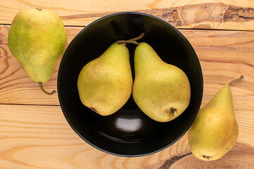 Four sweet juicy pears with a black dish on a wooden table , macro, top view.