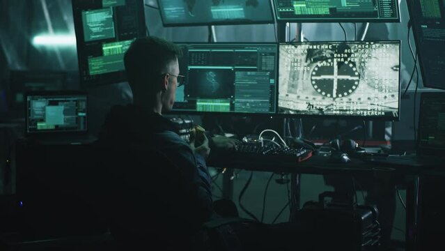 Young man eating donut and hacking process of spaceship and space station coupling docking while sitting at desk in dark room at night. Footage on the screeen furnished by NASA.