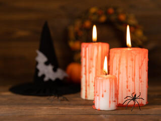 Composition of a group of scary bloody candles burning on a textured brown wood.Copy space on background.Witch hat with spider and bat. Black magic ritual or scary Halloween rite.DIY Halloween decor.