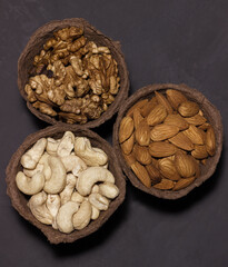 Three glasses of walnuts, almonds and cashews on a dark background. View from above.