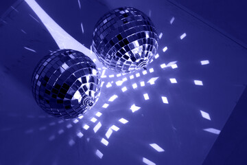 Two disco balls on wooden background with reflections, blue or Very Peri color lights