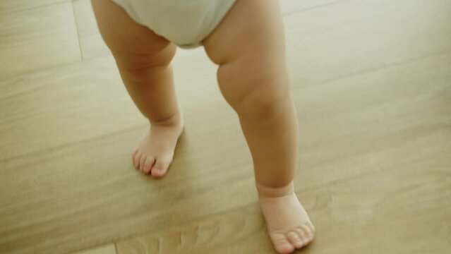 Close-Up Little Feet Walking On Warm Floor At Home, Baby Learning To Walk, Baby first steps Without Any Help. Toddler Exploring Home, Concept Newborn And Childhood, Slow Motion