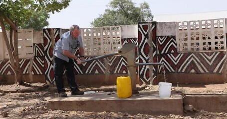 Man pumping water borehole well Sirigu northern Ghana. Poor poverty community where running water is not available. Fresh clean water from borehole well and carried to homes and businesses.