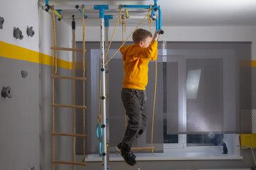 The boy pulls himself up on the horizontal bar at the sports complex at home in the room