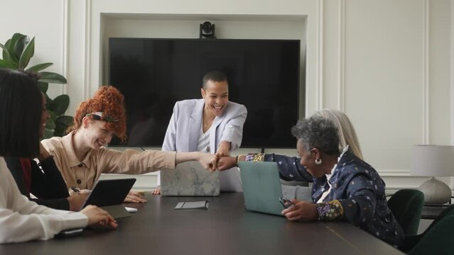 Slow motion of multi ethnic mixed age range businesswomen fist bumping in creative meeting