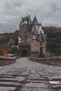 Cobblestone road on a bridge to the beautiful fairy-tale gothic medieval castle Burg Eltz. Autumn landscape in Germany - October 2021