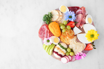 Spring or Easter theme charcuterie board against a white marble background. Variety of cheese,...