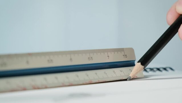 Hand of a man using a wooden pencil to draw lines on paper with an architectural scale and degree ruler