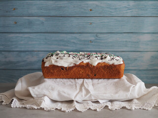 Easter cupcake with white icing and sprinkles on a towel with lace on a blue wooden background. Rustic pastries, Copy Spase