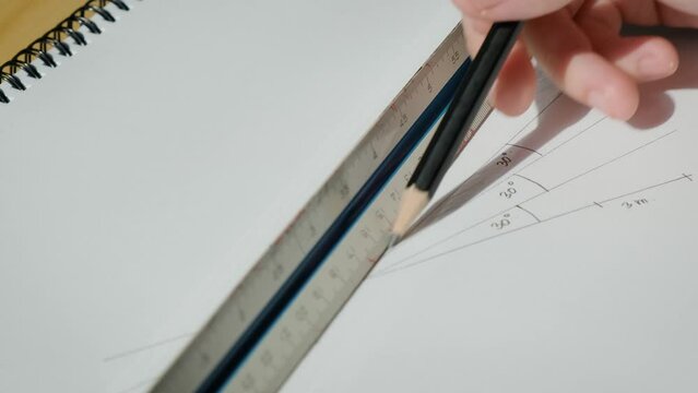 Hand of a man using a wooden pencil to draw lines on paper with an architectural scale and degree ruler