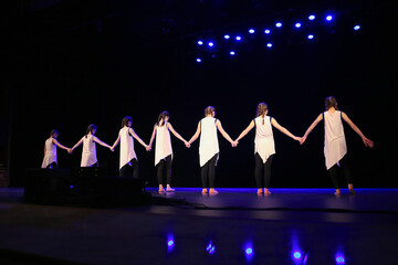 Girls dance on stage, they hold hands, stand with their backs