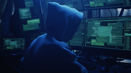 Anonymous hacker in hoodie writing code and explaining attack to associate while hacking stock market in dark room