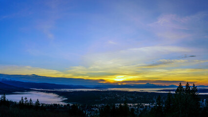 Sunrise over BC valley carpeted with low lying cloud inversion, with mountains in silhouette on horizon.