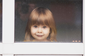Beautiful fair-haired baby looking out the window