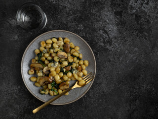 Plate with cooked potato gnocchi with butter sauce, mushrooms, spinach and cheese on dark background. Top view with copy space.