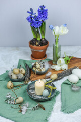 Dekoration Ostern mit Eiern, Federn und Frühlingsblumen auf einem Tisch mit Teller, Schale, Blumenvase und Holzbrett, Frühling dekorieren, Tulpe, Hyazinthe